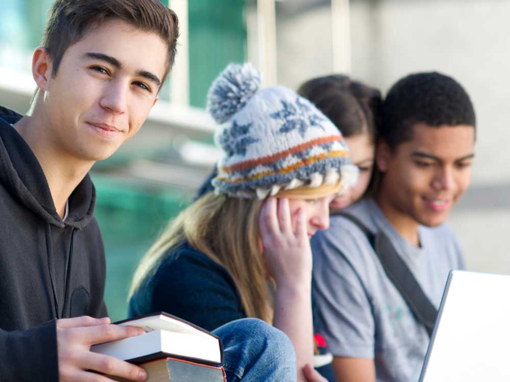 Students sitting in a group, holding books and a laptop computer.